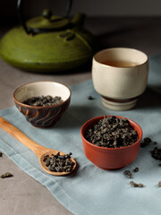 Green large-leaf tea powder in bowls, Chinese teapot in the background. Close-up. Vertical