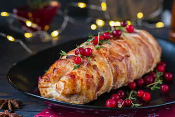 Cold appetizer, whole baked turkey and minced meat roll wrapped in bacon, on a black plate on a...