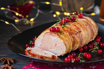 Cold appetizer, whole baked turkey and minced meat roll wrapped in bacon, on a black plate on a dark wooden background.