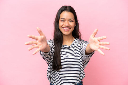 Young Colombian woman isolated on pink background presenting and inviting to come with hand
