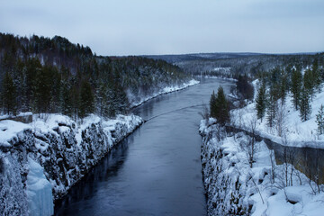Beautiful winter landscape with a river and coniferous forest. View from above. Cold frozen river. Aerial view of frozen river in winter forest with snowy trees. Winter nature