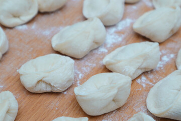 Fototapeta na wymiar Dumplings with meat. Vareniki Homemade. Flour, dough on a wodden background. Home cooking dumplings, dough and minced meat