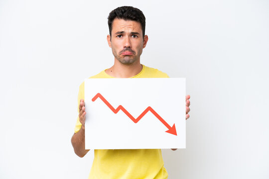Young handsome man over isolated white background holding a sign with a decreasing statistics arrow symbol with sad expression