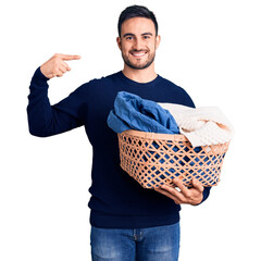 Young handsome man holding laundry basket pointing finger to one self smiling happy and proud