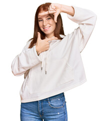 Young read head woman wearing casual sweatshirt smiling making frame with hands and fingers with happy face. creativity and photography concept.