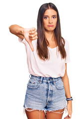 Young hispanic woman wearing casual white tshirt looking unhappy and angry showing rejection and negative with thumbs down gesture. bad expression.