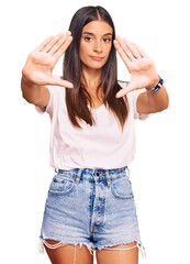 Obraz na płótnie Canvas Young hispanic woman wearing casual white tshirt doing frame using hands palms and fingers, camera perspective