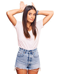 Young hispanic woman wearing casual white tshirt doing bunny ears gesture with hands palms looking cynical and skeptical. easter rabbit concept.