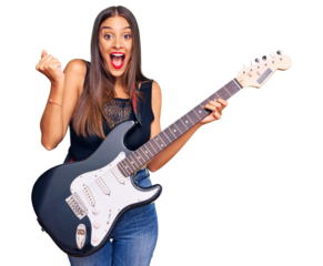 Young hispanic woman playing electric guitar screaming proud, celebrating victory and success very excited with raised arms