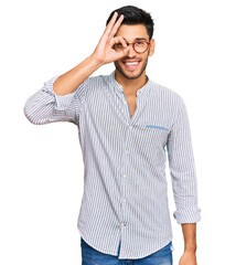 Young handsome man wearing casual clothes and glasses doing ok gesture with hand smiling, eye looking through fingers with happy face.