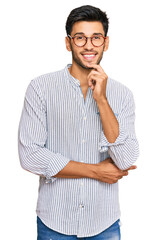 Young handsome man wearing casual clothes and glasses looking confident at the camera with smile with crossed arms and hand raised on chin. thinking positive.