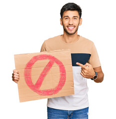 Young handsome man holding prohibited warning banner smiling happy pointing with hand and finger