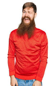 Redhead man with long beard wearing casual clothes winking looking at the camera with sexy expression, cheerful and happy face.