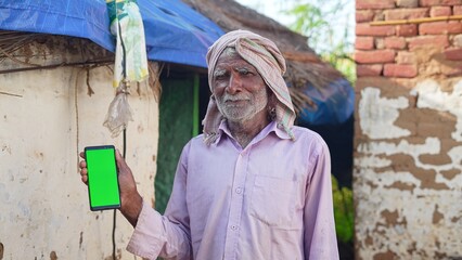 Indian old man holding a mobile phone and point towards it's screen. Mobile phone with a green screen for mockup.