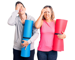 Couple of women holding yoga mat stressed and frustrated with hand on head, surprised and angry face