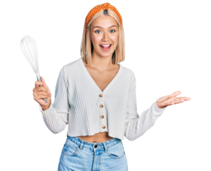 Beautiful young blonde woman holding baker whisk celebrating achievement with happy smile and winner expression with raised hand