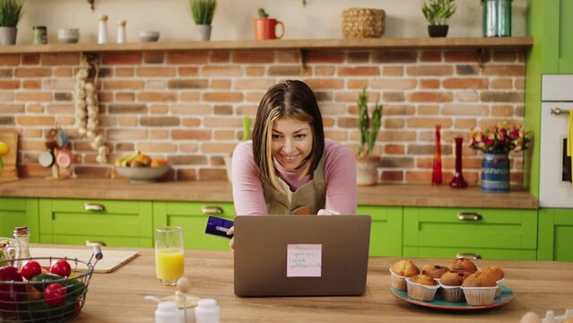 Modern kitchen happy house woman using the laptop to make a online shopping she watching something on the laptop and smiling large