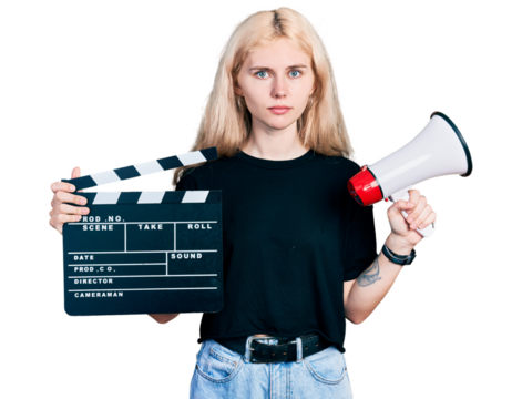 Young caucasian woman holding video film clapboard and megaphone relaxed with serious expression on face. simple and natural looking at the camera.