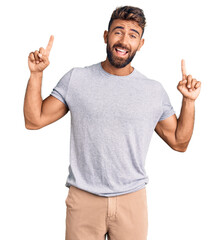 Young hispanic man wearing casual clothes smiling amazed and surprised and pointing up with fingers and raised arms.