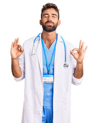 Young hispanic man wearing doctor uniform and stethoscope relax and smiling with eyes closed doing meditation gesture with fingers. yoga concept.