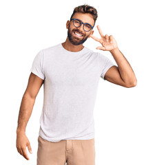 Young hispanic man wearing casual clothes and glasses doing peace symbol with fingers over face, smiling cheerful showing victory