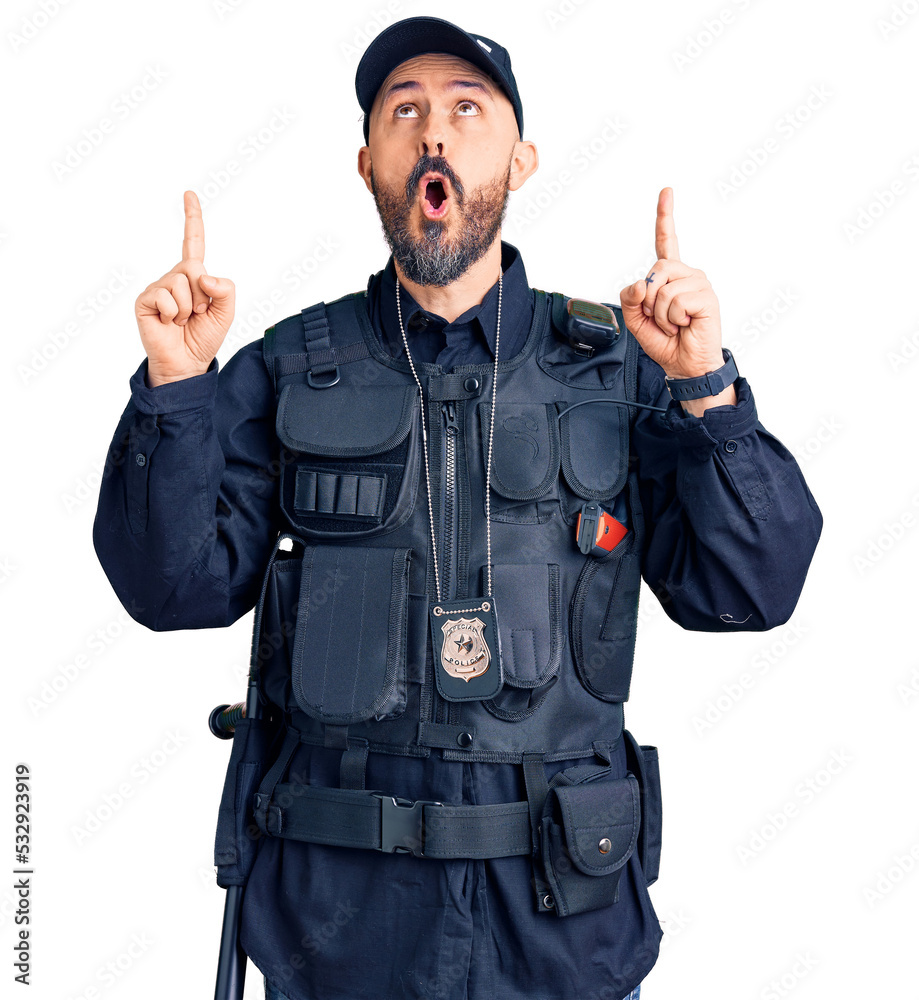 Canvas Prints young handsome man wearing police uniform amazed and surprised looking up and pointing with fingers 