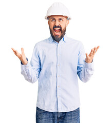 Young handsome man wearing architect hardhat crazy and mad shouting and yelling with aggressive expression and arms raised. frustration concept.