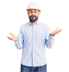 Young handsome man wearing architect hardhat clueless and confused expression with arms and hands raised. doubt concept.