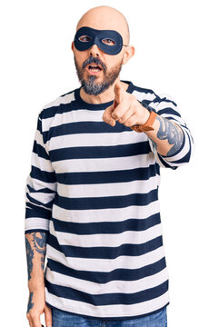 Young handsome man wearing burglar mask pointing displeased and frustrated to the camera, angry and furious with you