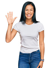 Beautiful hispanic woman wearing casual white tshirt showing and pointing up with fingers number five while smiling confident and happy.