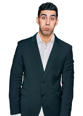 Handsome hispanic man wearing business clothes puffing cheeks with funny face. mouth inflated with air, crazy expression.
