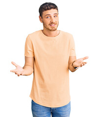 Handsome young man with bear wearing casual yellow tshirt clueless and confused expression with...