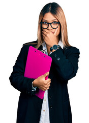 Young hispanic business woman holding clipboard with blank space shocked covering mouth with hands for mistake. secret concept.