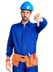 Young handsome man wearing worker uniform and hardhat afraid and terrified with fear expression stop gesture with hands, shouting in shock. panic concept.