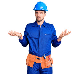 Young handsome man wearing worker uniform and hardhat doing bunny ears gesture with hands palms looking cynical and skeptical. easter rabbit concept.