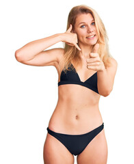 Fototapeta premium Young beautiful blonde woman wearing bikini smiling doing talking on the telephone gesture and pointing to you. call me.