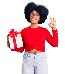 Young african american girl holding gift smiling positive doing ok sign with hand and fingers. successful expression.