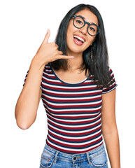 Beautiful asian young woman wearing casual clothes and glasses smiling doing phone gesture with hand and fingers like talking on the telephone. communicating concepts.