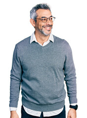 Middle age hispanic with grey hair wearing glasses looking away to side with smile on face, natural...