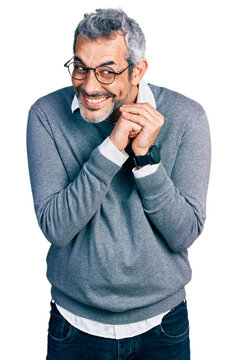 Middle age hispanic with grey hair wearing glasses laughing nervous and excited with hands on chin looking to the side