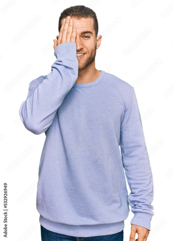 Sticker Young caucasian man wearing casual clothes covering one eye with hand, confident smile on face and surprise emotion.