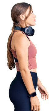 Beautiful caucasian young woman wearing gym clothes and using headphones looking to side, relax profile pose with natural face and confident smile.