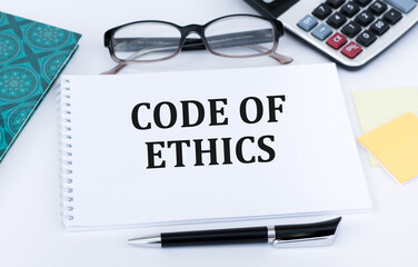 CODE OF ETHICS is written on a white card next to a potted flower, diaries and calculator. Organizational concept