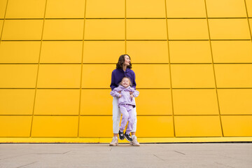 Woman in purple hoody have fun with cute girl 4-5 years old. Mommy and little daughter on yellow mall wall background. Childhood concept of love for family and fatherhood on Mother's Day