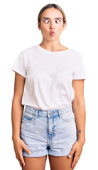 Obraz premium Young beautiful blonde woman wearing casual white tshirt making fish face with lips, crazy and comical gesture. funny expression.