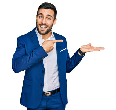 Young hispanic man wearing business jacket amazed and smiling to the camera while presenting with hand and pointing with finger.