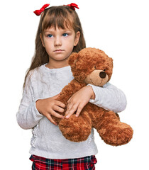 Little caucasian girl kid hugging teddy bear stuffed animal thinking attitude and sober expression...