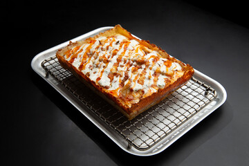 detroit pizza on an iron tray on a dark background.