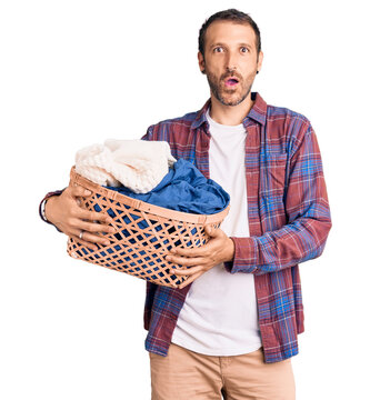 Young handsome man holding laundry basket scared and amazed with open mouth for surprise, disbelief face