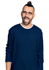 Hispanic man with ponytail wearing casual sweater and glasses sticking tongue out happy with funny expression. emotion concept.